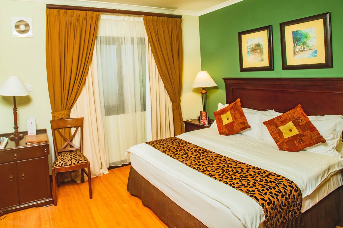 Une chambre d’hôtel avec un lit, un bureau, une chaise, une télévision et une fenêtre avec des rideaux.