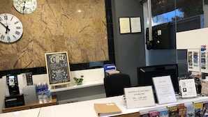 Un mostrador de recepción con una máquina de café, botellas de agua, un menú en una pizarra y entradas para atracciones de Singapur.