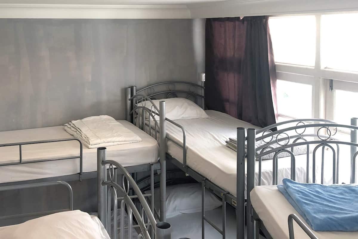 A room with three metal bunk beds, a grey wall, and a window with curtains.