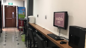 Un escritorio de madera largo con una computadora, que incluye un monitor, teclado y ratón. Varias sillas negras están frente al escritorio. Un refrigerador de Coca-Cola está en el suelo junto al escritorio.