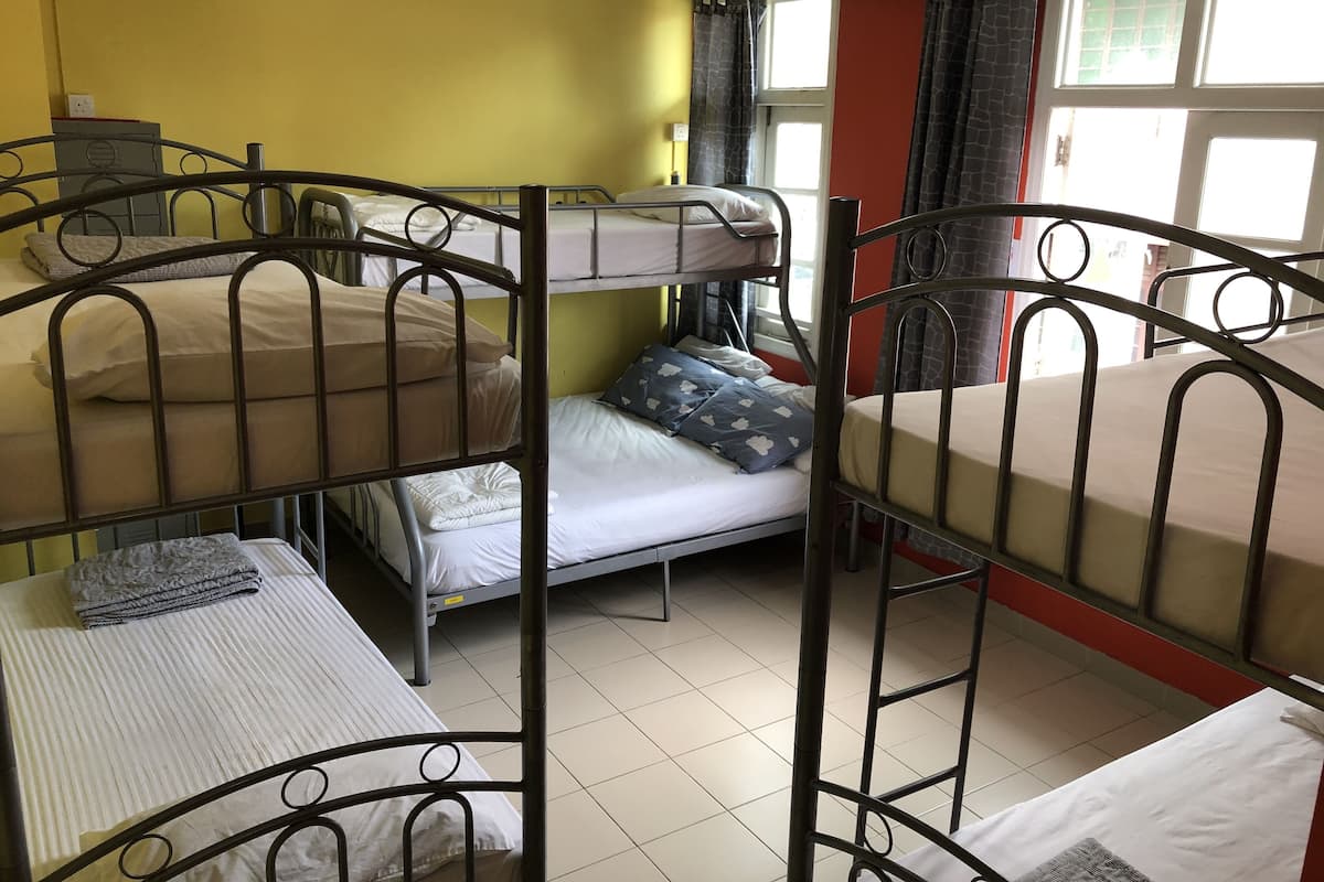 A dormitory room with bunk beds, a small table, and a window with curtains.