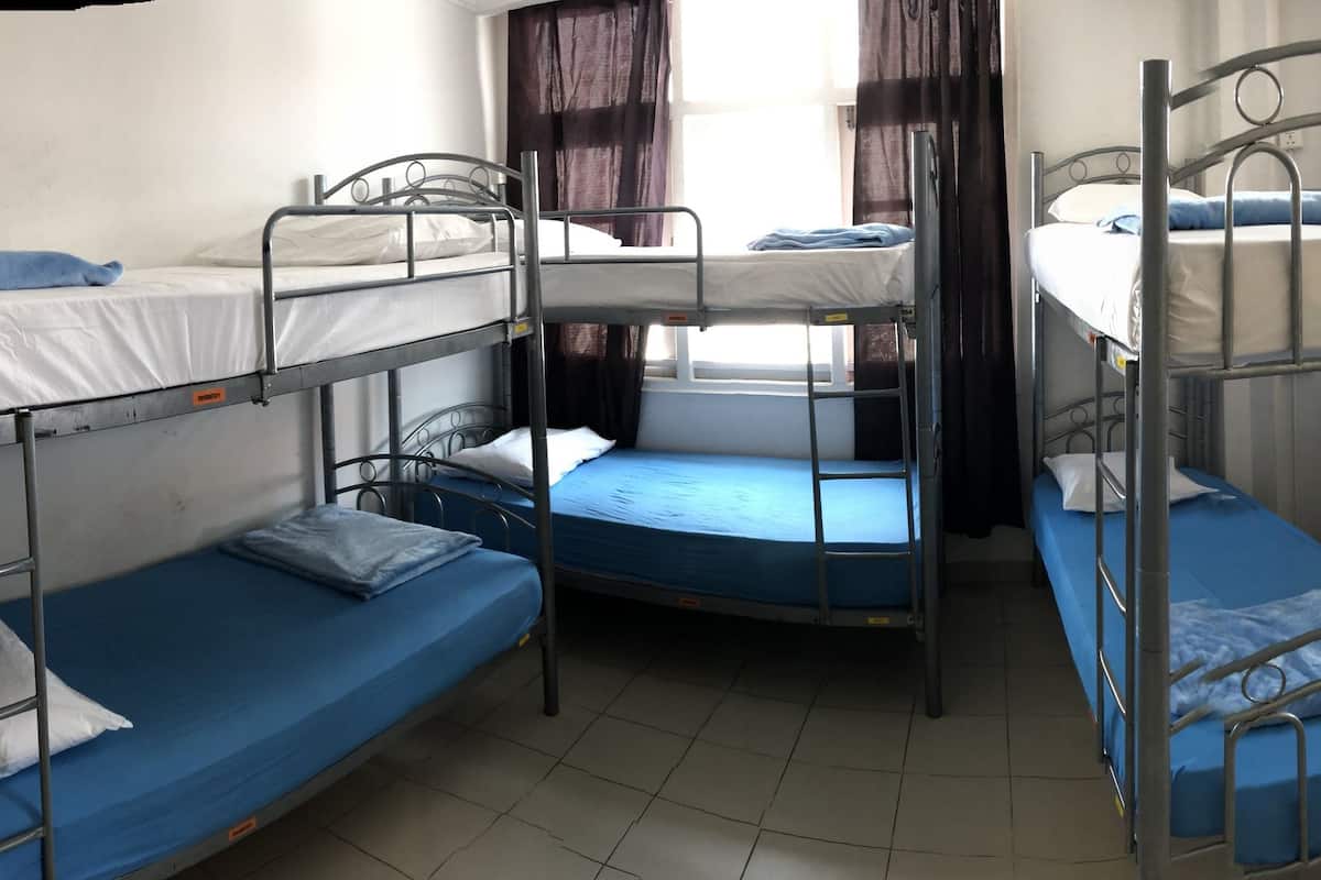 A dormitory room with bunk beds, a window with curtains, and a set of lockers.