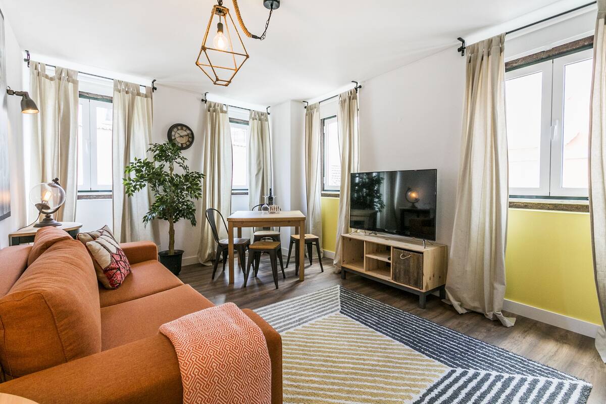 Ein Wohnzimmer mit Sofa, Fernseher, Esstisch, Stühlen und einer Topfpflanze.