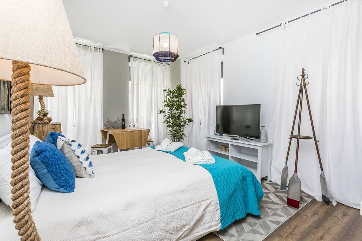 Ein Hotelzimmer mit Bett, Fernseher, Schreibtisch, Pflanze und Stativ.