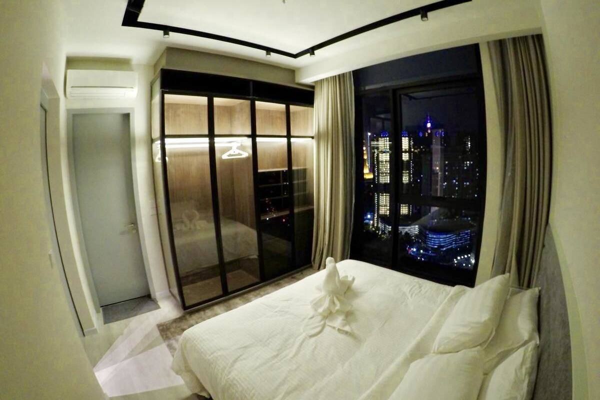 A hotel room with a bed, a sliding door to a balcony, and a city view at night.