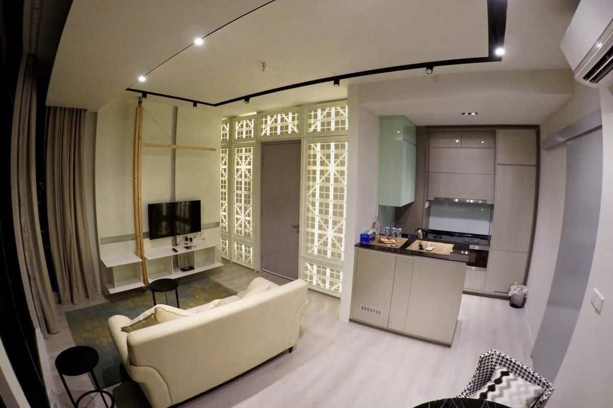 A modern living room with a sofa, TV, and a kitchen area with cabinets and a countertop.