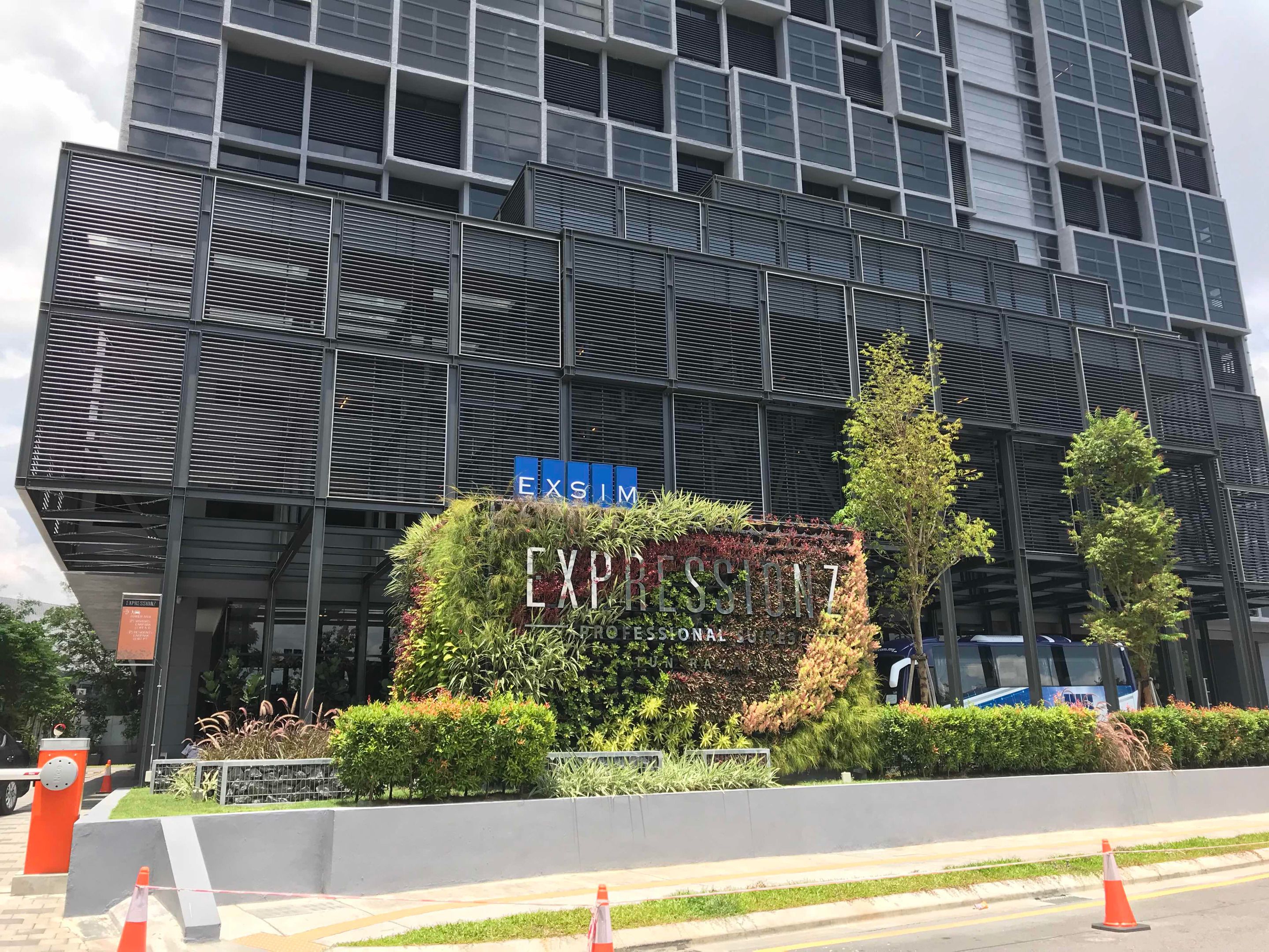 A modern building with a large sign reading "EXPRESSIONZ" and a landscaped area with plants in front.