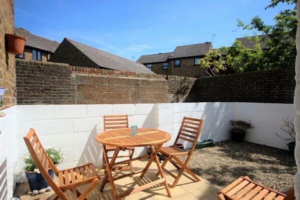 A patio with a round wooden table and four chairs, surrounded by a white wall and a brick wall.