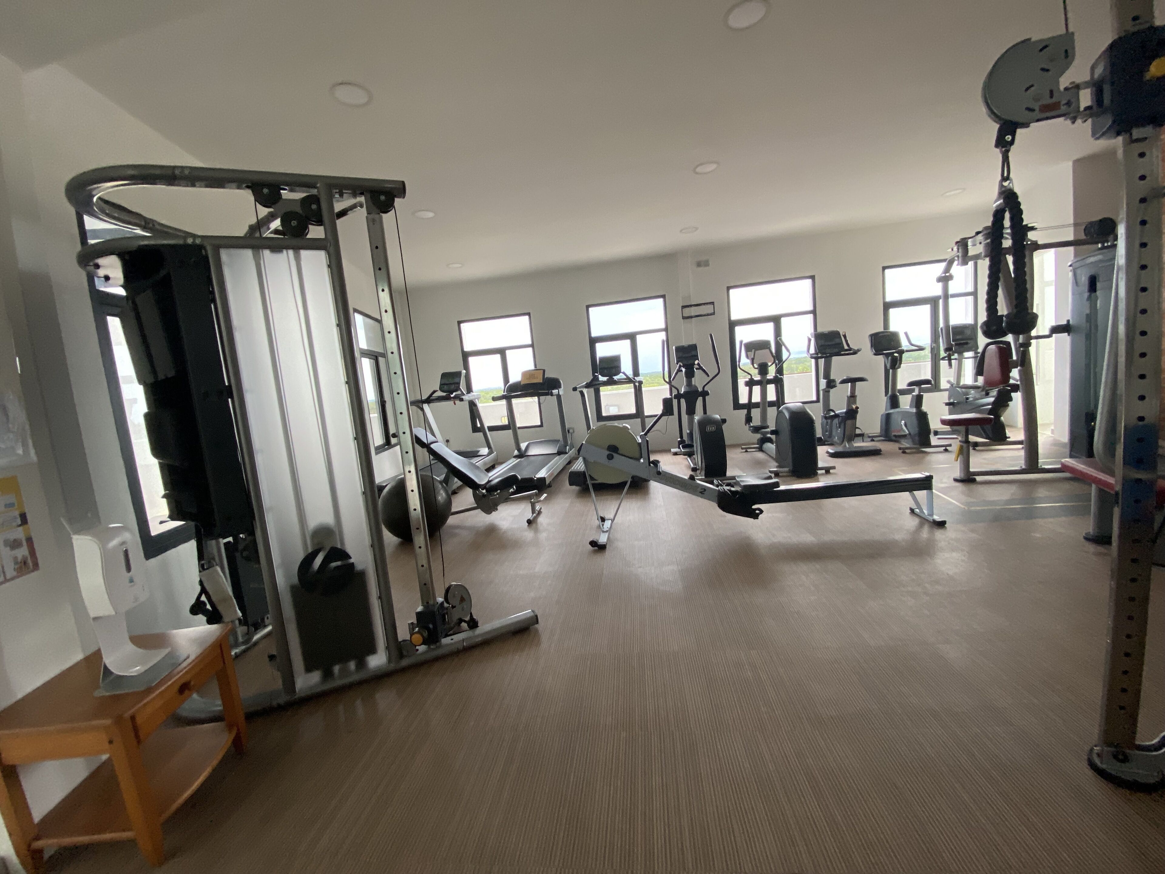 A gym with various exercise equipment, large windows, and a wooden floor.