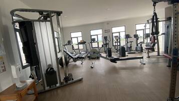 Un gimnasio con diverso equipo de ejercicio, amplias ventanas y piso de madera.