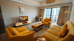 A modern hotel room with a living area featuring yellow sofas, a flat-screen TV, a dining table, and a balcony with curtains. - The Lanes Hotel (Tutong)