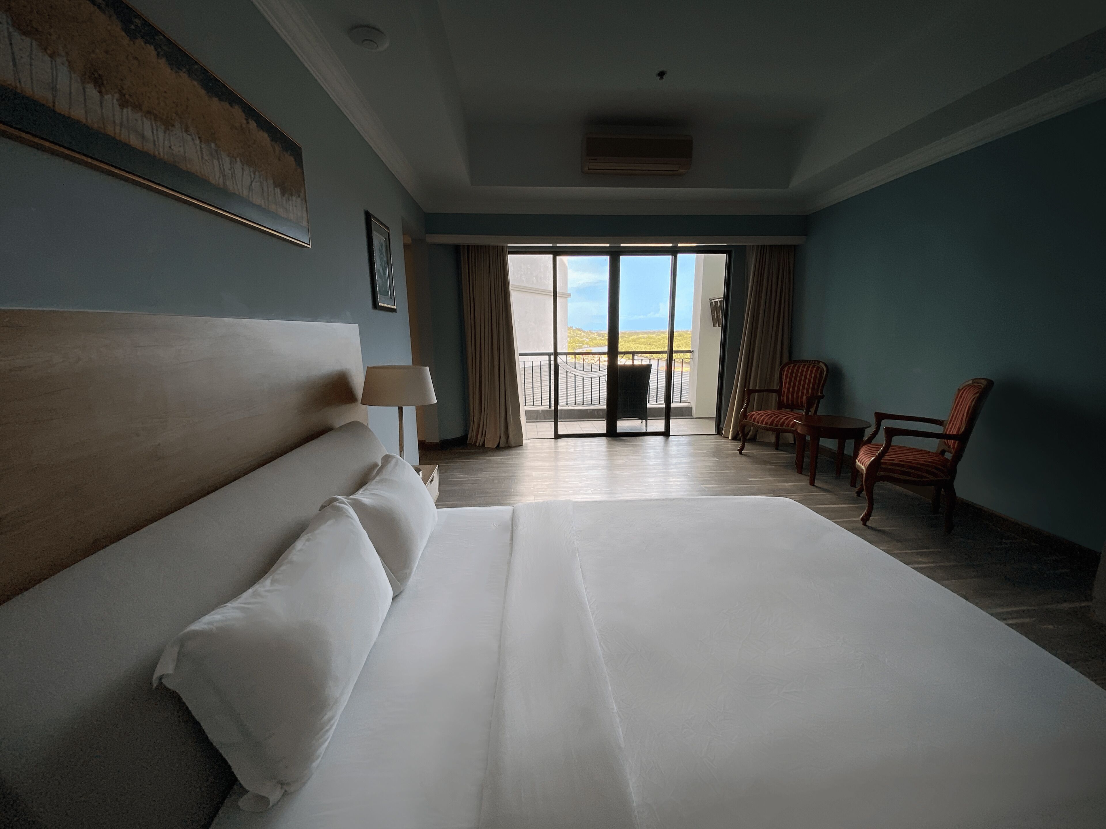 A hotel room with a large bed, a chair, a lamp, and a view of the outdoors.