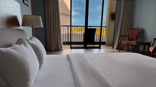 A hotel room with a large bed, a chair, a table, and a view of the outdoors. - The Lanes Hotel (Tutong)