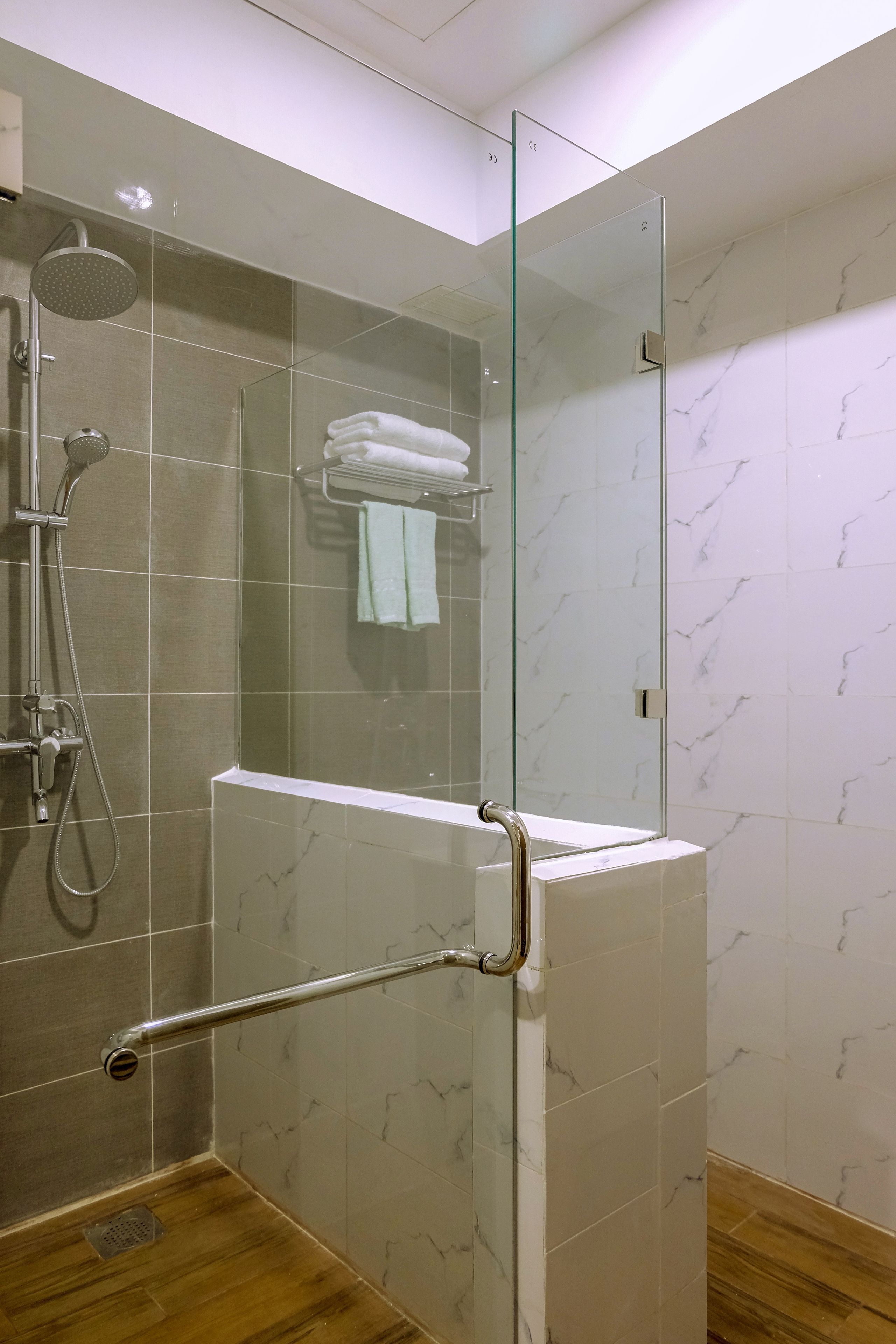 Un espacio de ducha moderno con puerta de vidrio, cabezal de ducha de mano y un perchero con toallas dobladas.
