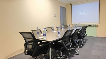A conference room with a long table, black chairs, water bottles, and a projector screen displaying "The Lane's Hotel" logo.