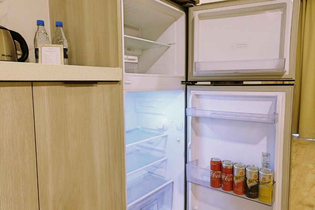 A hotel room with a double-door refrigerator, a minibar, and a shelf with bottled water and canned drinks.