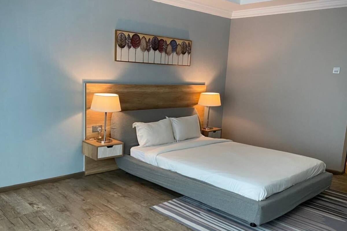 Une chambre à coucher moderne avec un lit, deux lampes de chevet, une tête de lit et un élément décoratif mural.