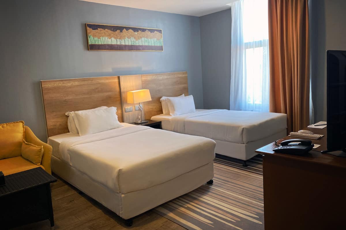 Une chambre d’hôtel avec deux lits, un bureau, une chaise, une lampe et un tableau au mur.