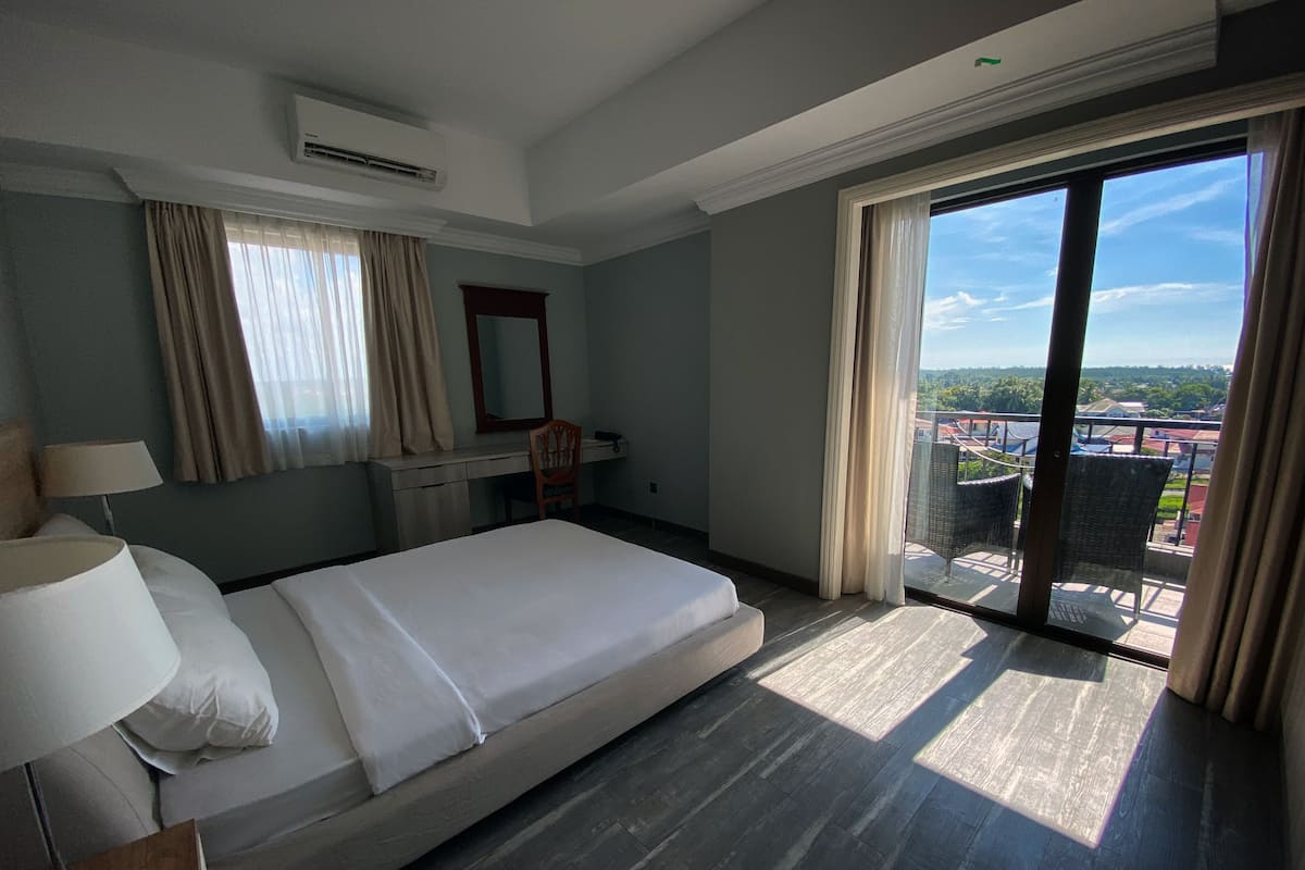 Une chambre d’hôtel équipée d’un lit, d’un bureau, d’une chaise, d’une grande fenêtre donnant sur des immeubles et d’un appareil de climatisation.