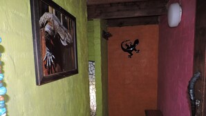 A hallway with a green wall, a framed picture of a snake, a black sculpture, and a staircase leading to a room with a red wall. - Kruger Inn Backpackers (Nkomazi)