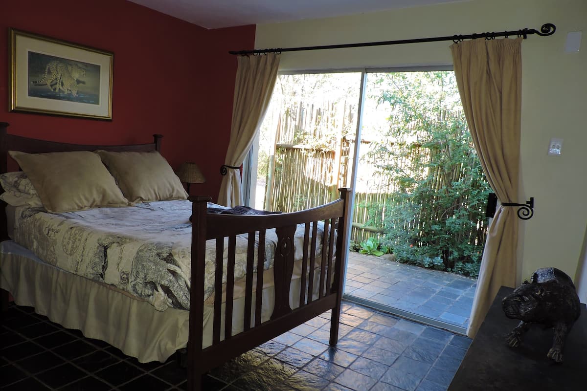 A bedroom with a bed, a wooden chair, a nightstand, and a view of a garden through a sliding door.
