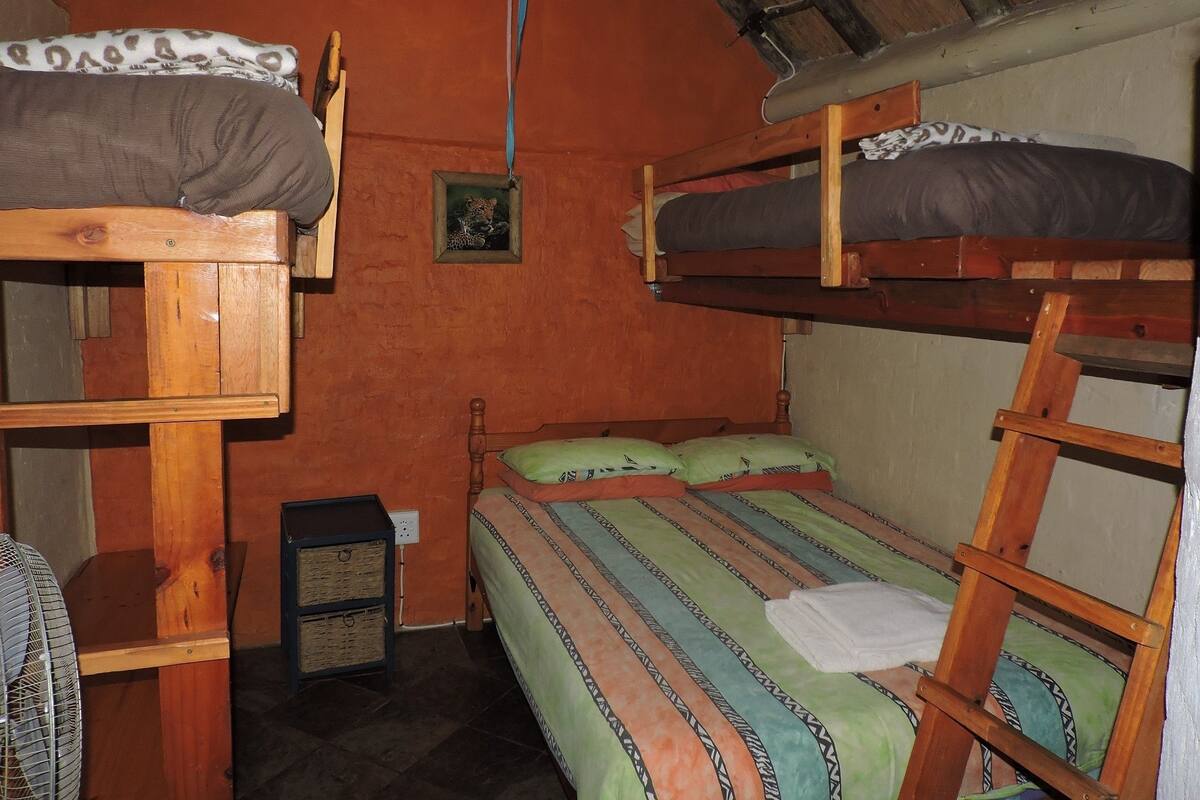 A dormitory room with bunk beds, a small shelf with baskets, and a fan.