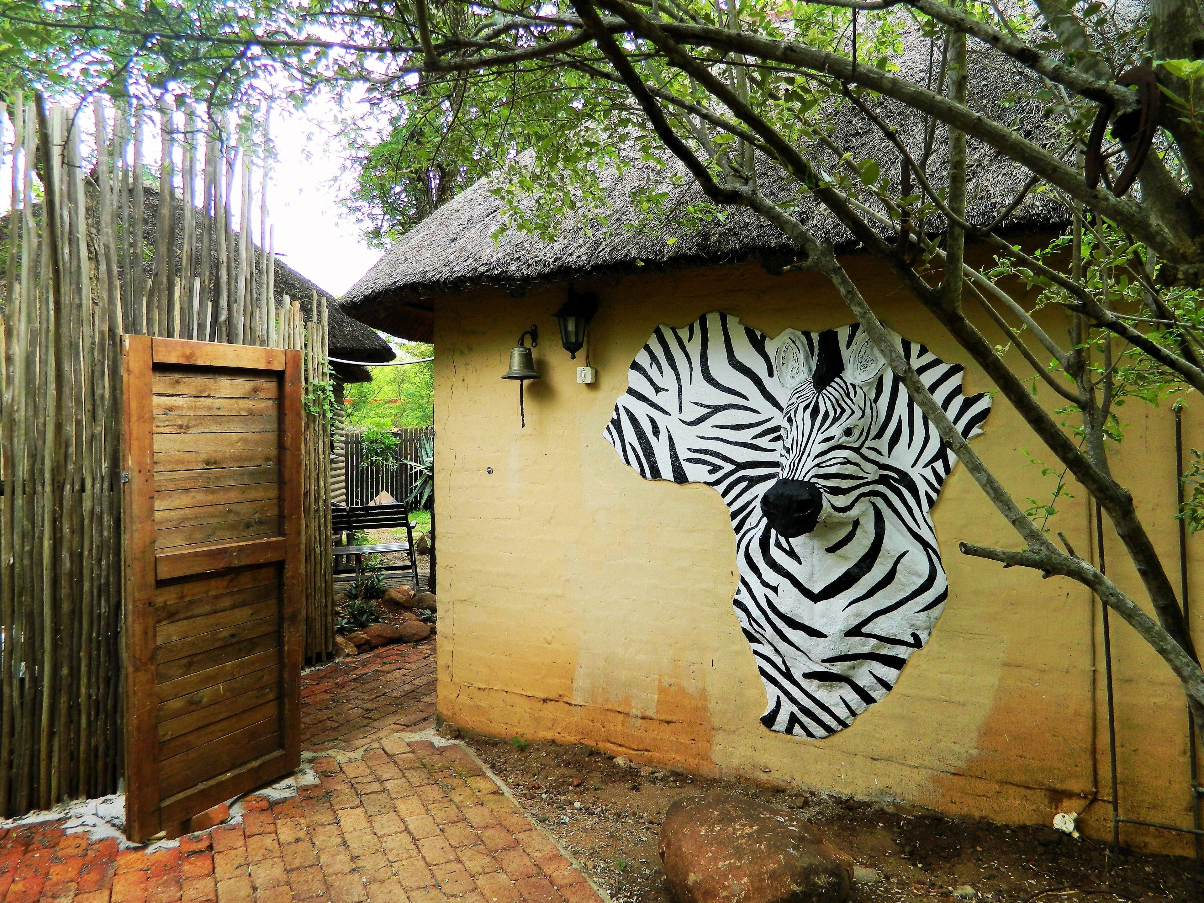 A rustic building with a zebra mural, a wooden door, and a brick pathway.