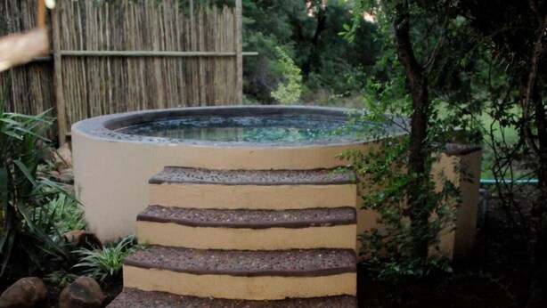 A circular water feature with a tiered stone structure in a garden setting. - Kruger Inn Backpackers (Nkomazi)