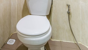 Un WC in un bagno con piastrelle color beige e un tubo doccia.