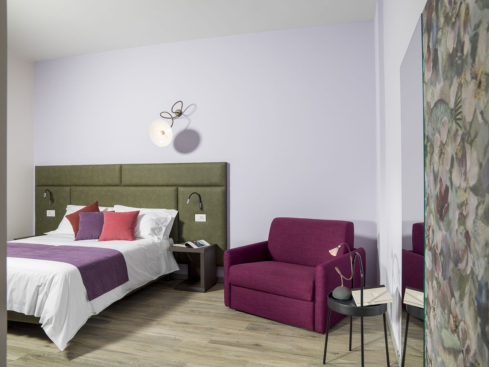 A modern hotel room with a green upholstered bed, white bedding, and a purple armchair.