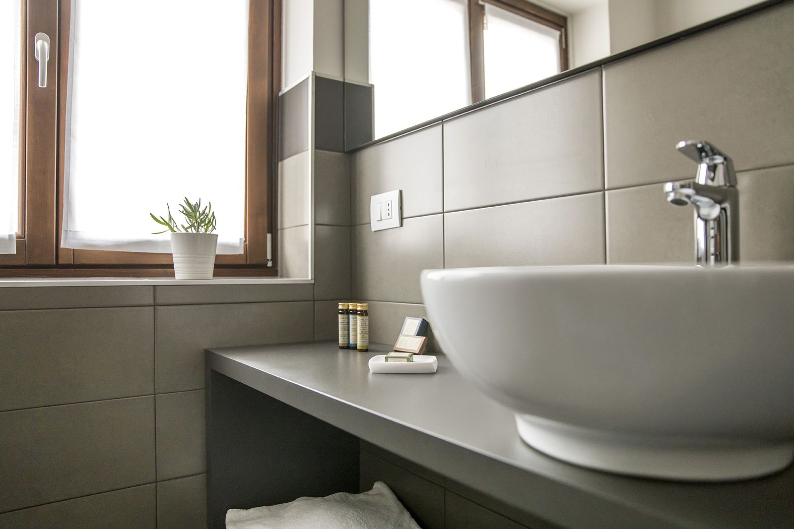 A modern bathroom with a large white sink, a mirror, and a window with a plant.