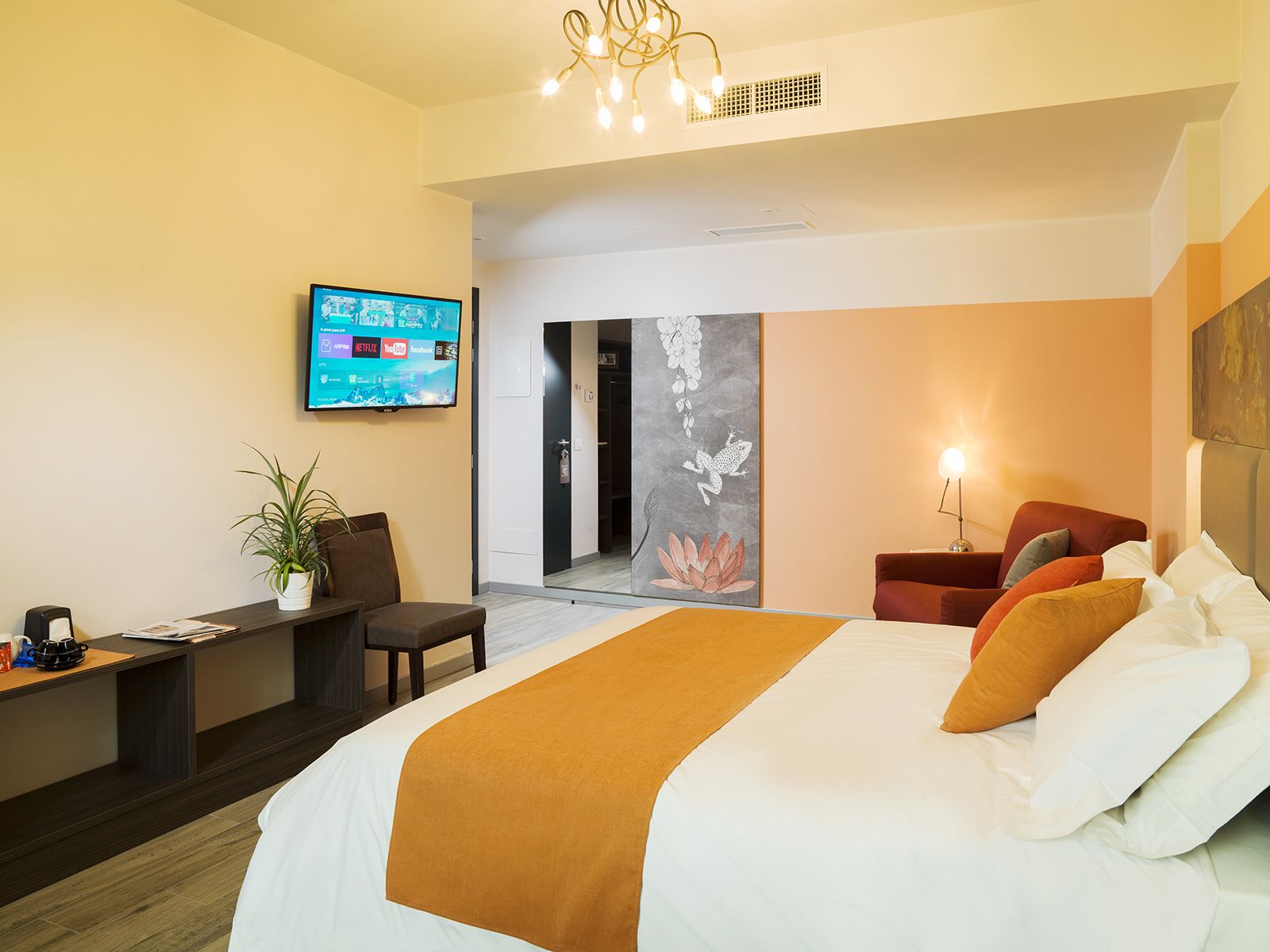 A modern hotel room with a large bed, a desk with a laptop, a television, and a door leading to a bathroom.