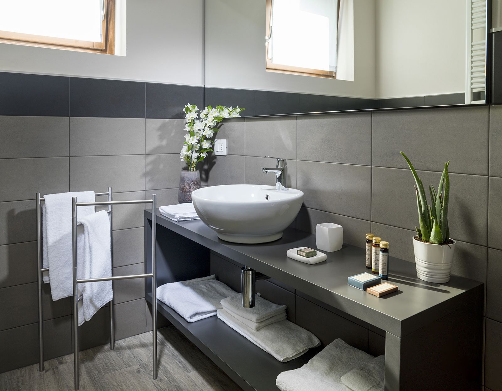 A modern bathroom with a large white sink, a towel rack, a potted plant, and a mirror.