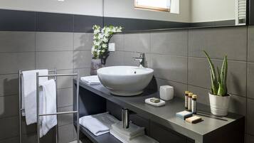 A modern bathroom with a large white sink, a towel rack, a potted plant, and a mirror.