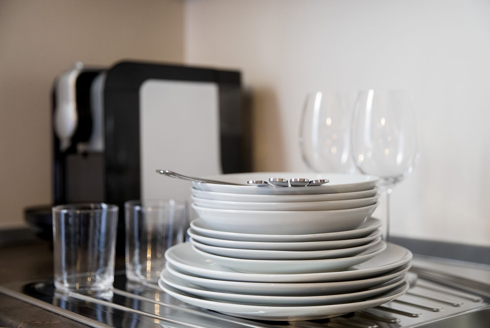 A stack of white plates and bowls on a tray, with a coffee machine and glasses in the background.
