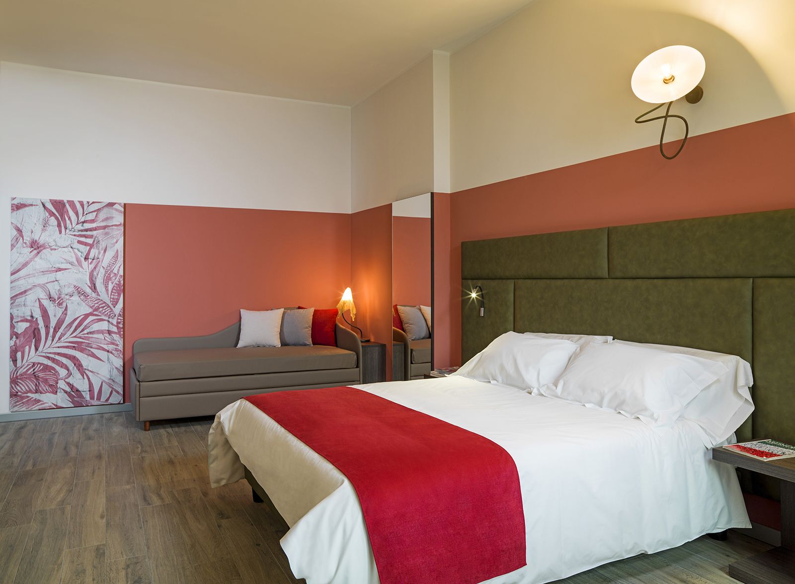 Una habitación de hotel con cama, sofá, mesita de noche y lámpara de pared.