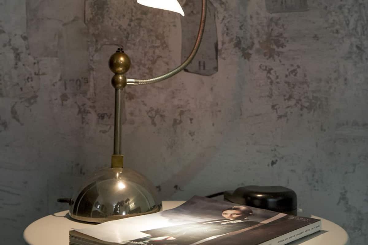 Un tavolo con una lampada, un libro e un piccolo oggetto sopra.