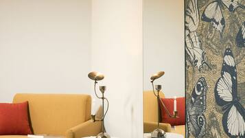 A modern living room with a sofa, two side tables, and a large mirror reflecting a butterfly-patterned wall.