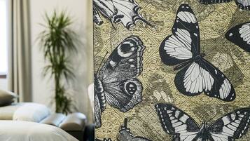 A hotel room with a bed, a plant, and a wall with a butterfly pattern.