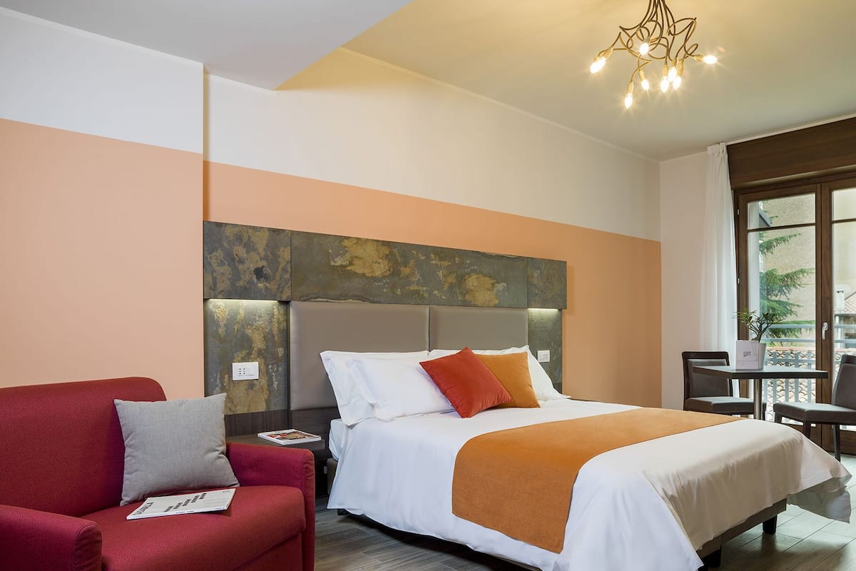 Una camera d'albergo con un letto, un divano rosso, un tavolino e una finestra con vista.