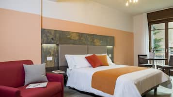 A hotel room with a bed, a red sofa, a small table, and a window with a view.