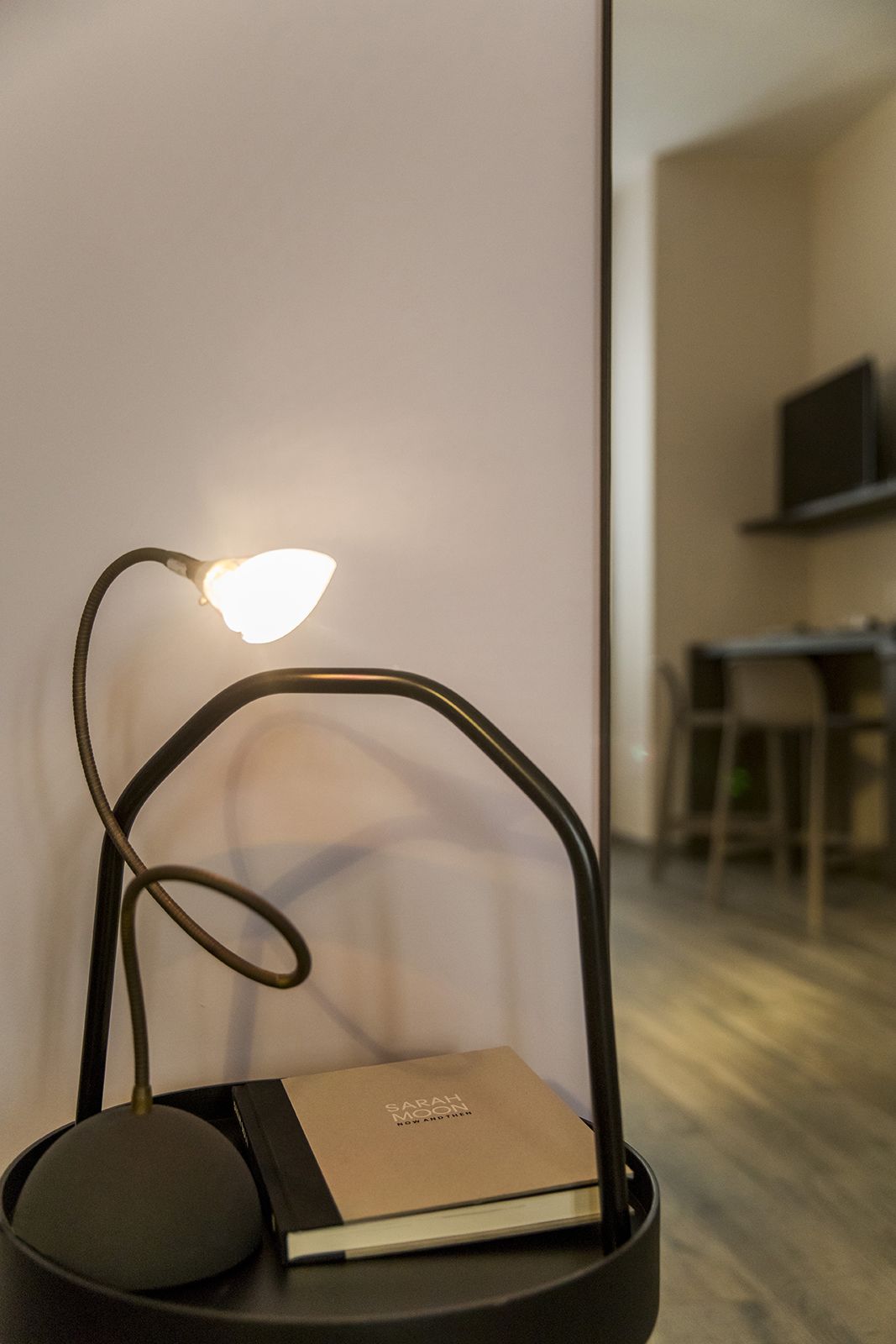 A modern desk lamp with a flexible neck and a book titled "Sarah Moon" on a black stand.