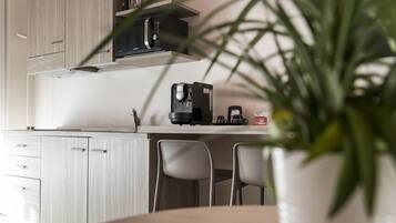A modern kitchen with a built-in microwave, coffee maker, and wine glasses on a shelf. There are two chairs and a potted plant in the foreground.