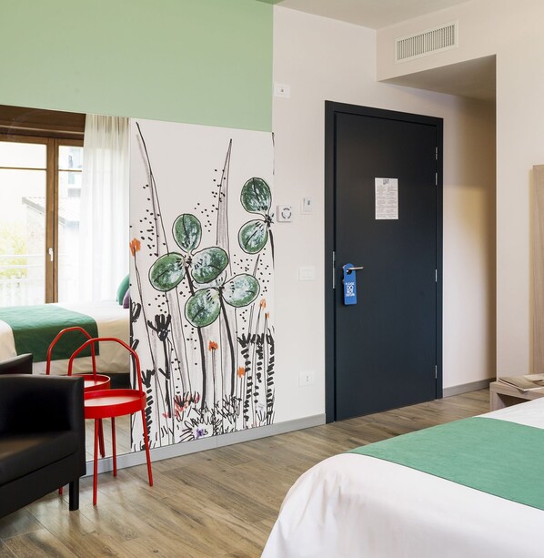 A hotel room with a bed, a desk, a chair, and a wall with a botanical mural.