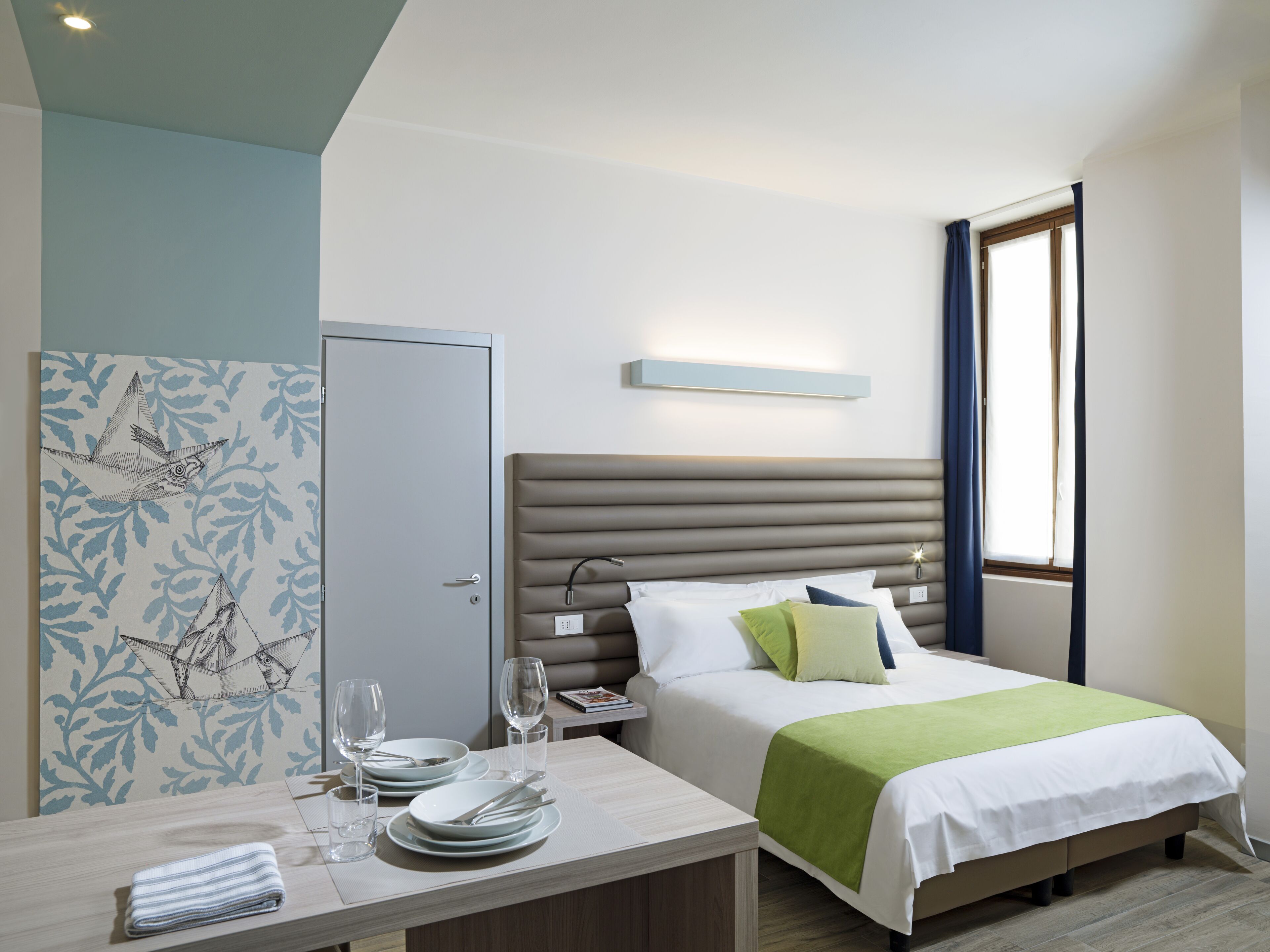 A hotel room with a bed, bedside table, and a window with curtains.