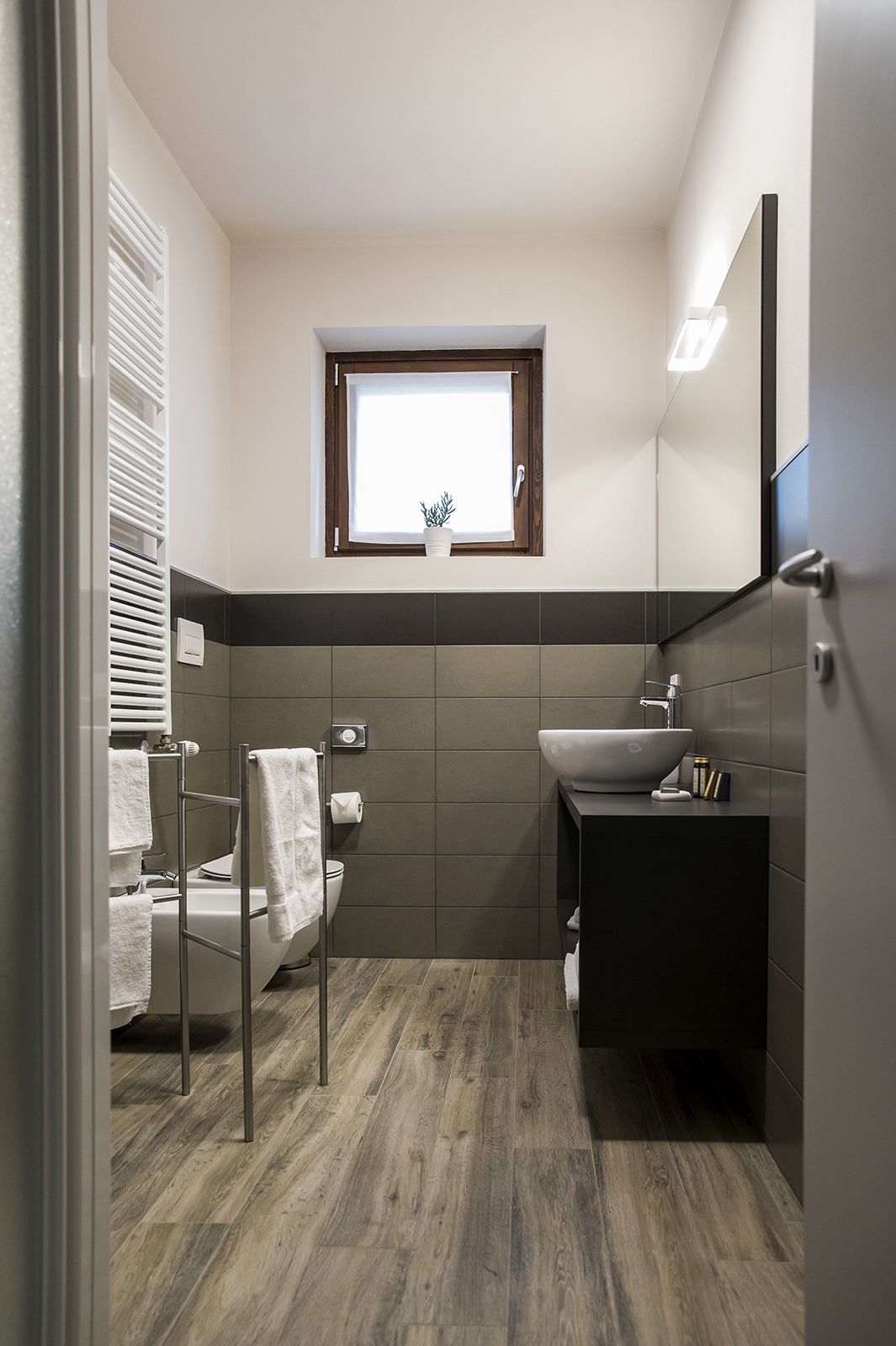 A modern bathroom with a toilet, bidet, and sink. There is a window above the sink and a towel rack next to the toilet.