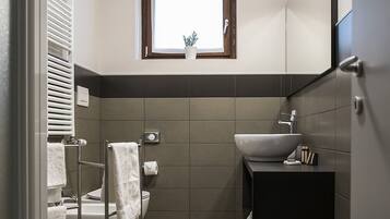 A modern bathroom with a toilet, bidet, and sink. There is a window above the sink and a towel rack next to the toilet.