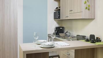 A compact kitchen with a microwave, coffee maker, and a small sink. There is a dining area with a table set for two, and a chair.
