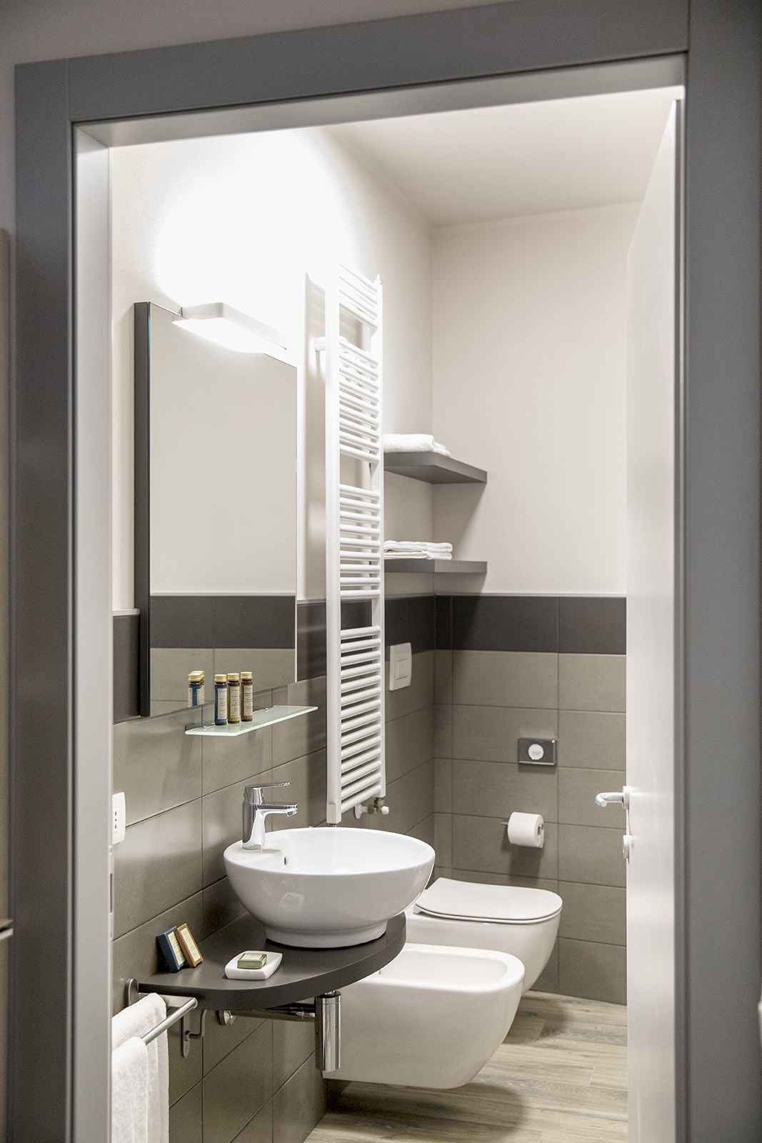 A modern bathroom with a large mirror, a white sink, a toilet, and a towel rack.