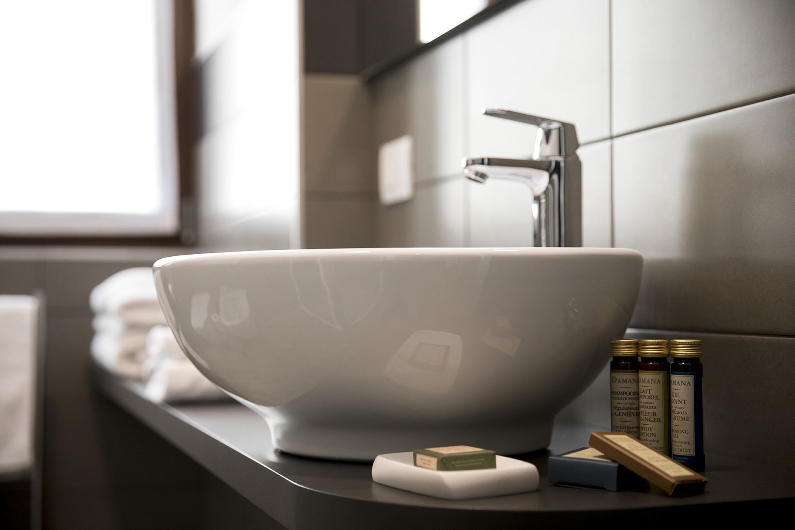 A modern bathroom with a large white basin, a faucet, and toiletries on the counter.